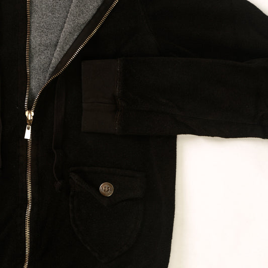 close-up of women's black velvety fabric jacket with drawstring hood and two front pockets with metal buttoned flaps with cuffed sleeves and hemming and full-length metal zipper